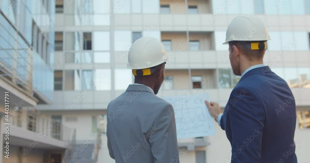 Back view of diverse industrial engineers planning on blueprint at work site. Back view of diverse industrial engineers planning on blueprint at work site.