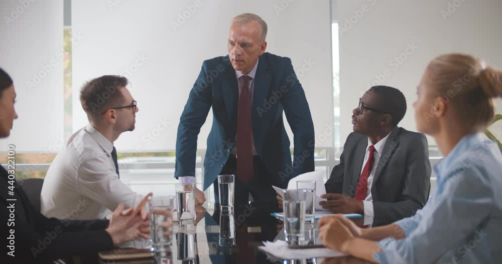 Team of diverse workers listening to senior manager sitting around office table in corporate meeting