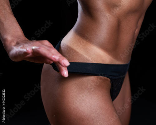 A faceless woman in black panties shows off the result of an instant tan