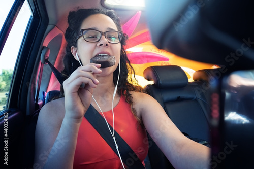girl brunette with headphones eating ice cream in the car. Female teenager in eoral dress, eats ice cream while in the car during a road trip