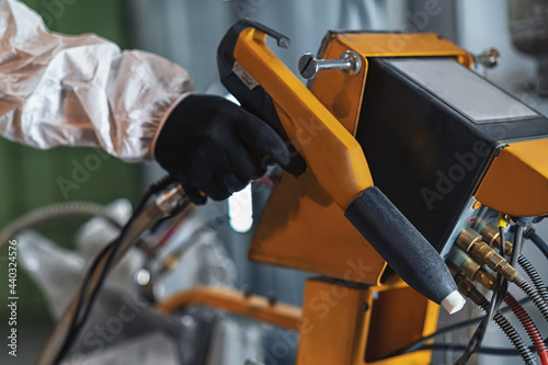 A worker's hand in protective clothing holding a powder coating sprayer