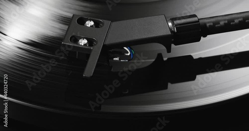 Extreme closeup of turntable's tonearm headshell lowering on spinning vinyl record photo