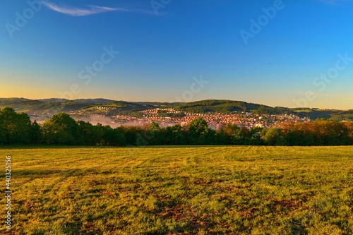 Sunrise over the meadow and in the background you can see the city and the hills
