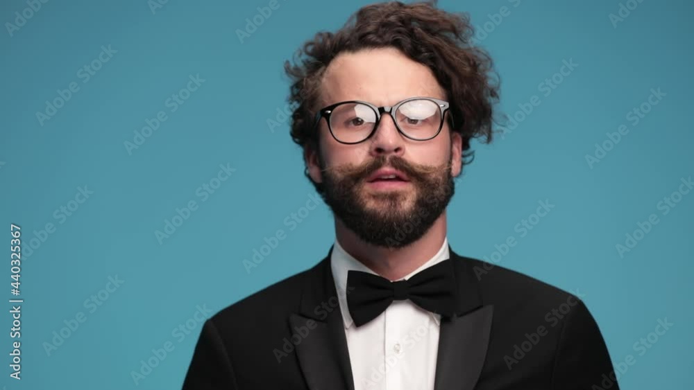 sexy long bearded guy with moustache wearing tuxedo and eyeglasses, making a snapping finger gesture and nodding against blue background in studio sexy long bearded guy with moustache wearing tuxedo and eyeglasses, making a snapping finger gesture and nodding against blue background in studio