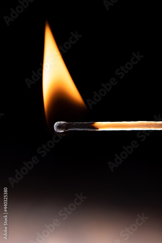 Triangular flame on a burning match against a black background.