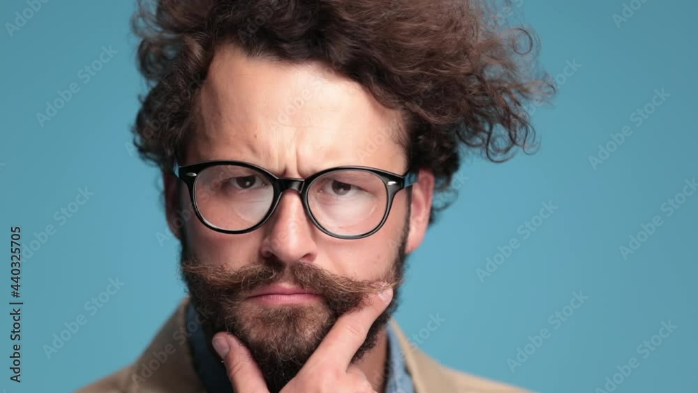 close up of casual guy with moustache and beard having an idea, thinking while rubbing beard and nodding on blue background in studio close up of casual guy with moustache and beard having an idea, thinking while rubbing beard and nodding on blue background in studio