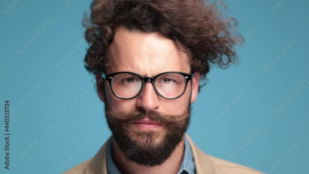 close up of serious casual man with moustache and eyeglasses standing and deeply looking while thinking on blue background in studio close up of serious casual man with moustache and eyeglasses standing and deeply looking while thinking on blue background in studio