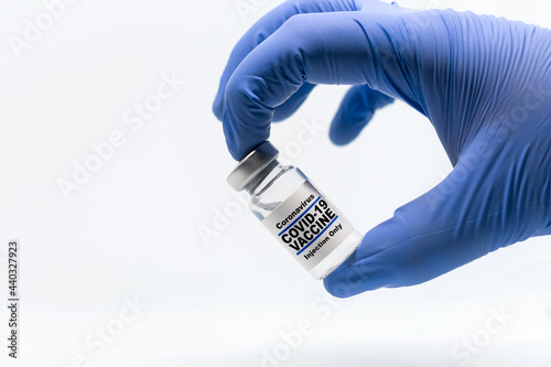 Health care cure concept with a hand in blue medical gloves holding vial bottle of Covid-19, Coronavirus, SARS-CoV-2 vaccine. Infinite white background.