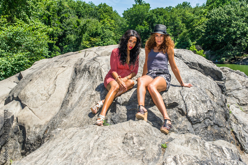Two sisters with two personalities, strong and soft, long brown curly hair and long black curly hair, is relaxing on big rocks..