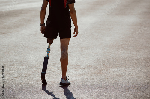 Rear view of sportsman with leg prosthetic standing on running track at the stadium.