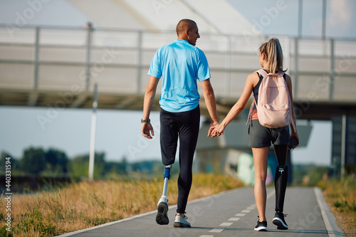 Fototapeta Naklejka Na Ścianę i Meble -  Rear view of disabled athletic couple with artificial legs holding hands while taking a walk outdoors.