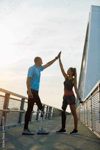 Happy athletic man and woman with disability giving high five to each other after successful training outdoors. © Drazen