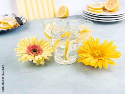 Lemon water drink with ice cubes on stone background with gerbera daisy yellow flowers