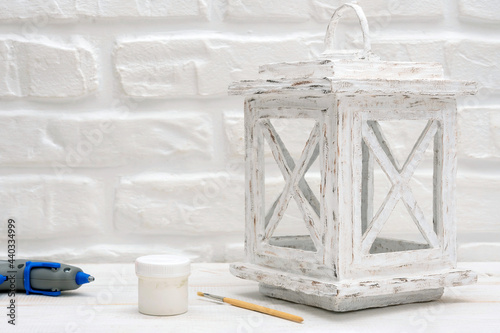 Decorative carton lantern with a piece of cardboard, glue gun and hot glue on a white wooden table.