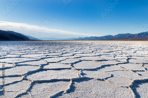 Sunrise over Badwater Basin, Death Valley, California. Sunburst over the far mountains; the basin floor is covered with white salt deposits; snaking crystal formations form hexagonal shapes.