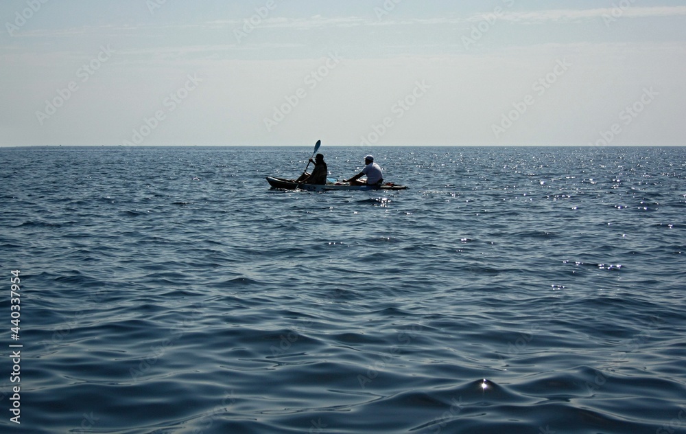 Two people row in the distance on a boat on the open sea.