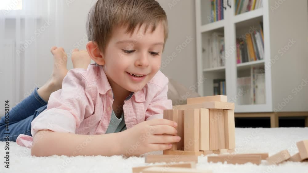 Smiling boy lying on floor and building house or tower from wooden blocks. Concept of child education and games at home Smiling boy lying on floor and building house or tower from wooden blocks. Concept of child education and games at home