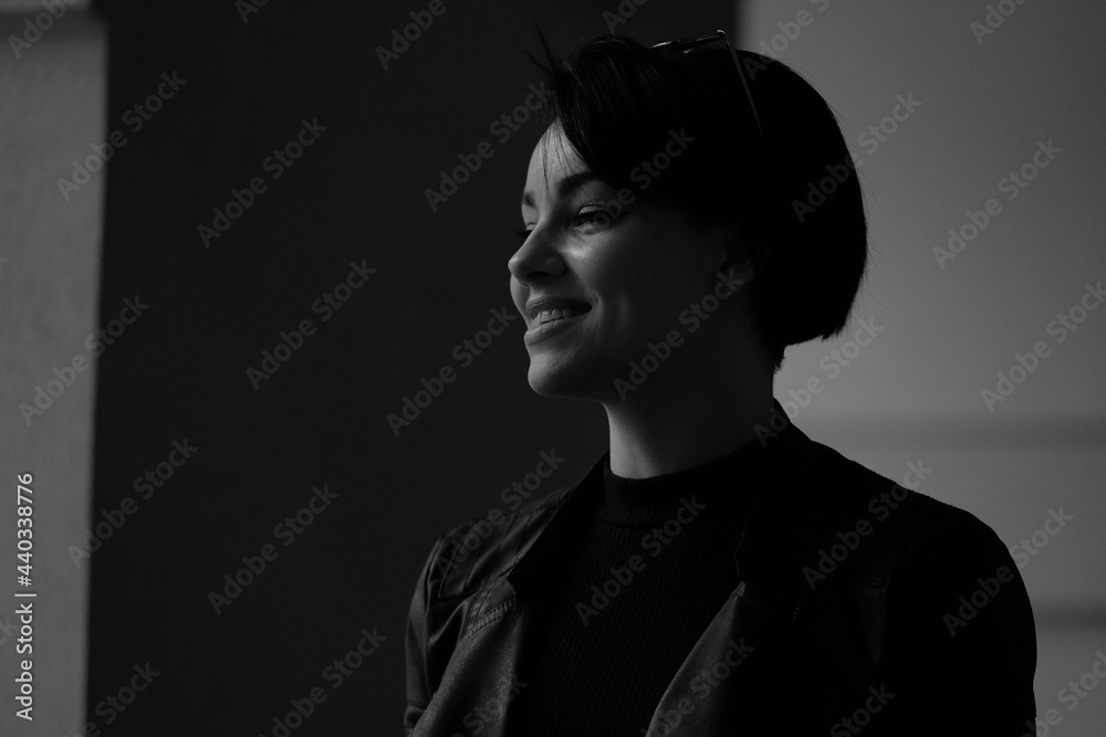 A happy young girl in a black leather jacket and short hair is sitting at a table. Black and white portrait of a smiling woman	
