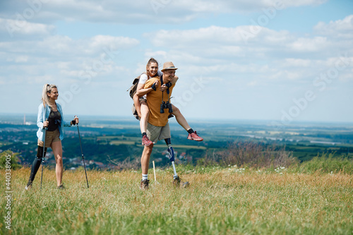 Group of young friends having fun while hiking in nature. Man with leg disability is carrying his female friend on his back.