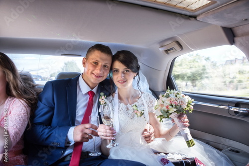  The bride and groom drink wine from glasses in the salon of a wedding car
