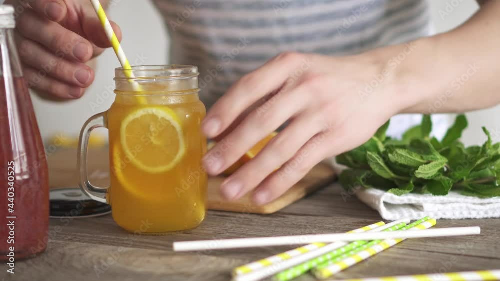 Man prepares refreshing cocktail at home kitchen. Citrus fruits on cutting bamboo board. Oranges and lemons in the background. Fresh sprigs of mint on white towel. Cocktail tube in glass with handle.
