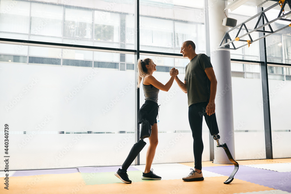 Happy athletic man and woman with leg disability greeting each other during sports training at gym.