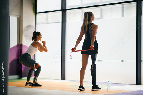 Sportswoman with leg disability and her friend working out with resistance band in a gym.