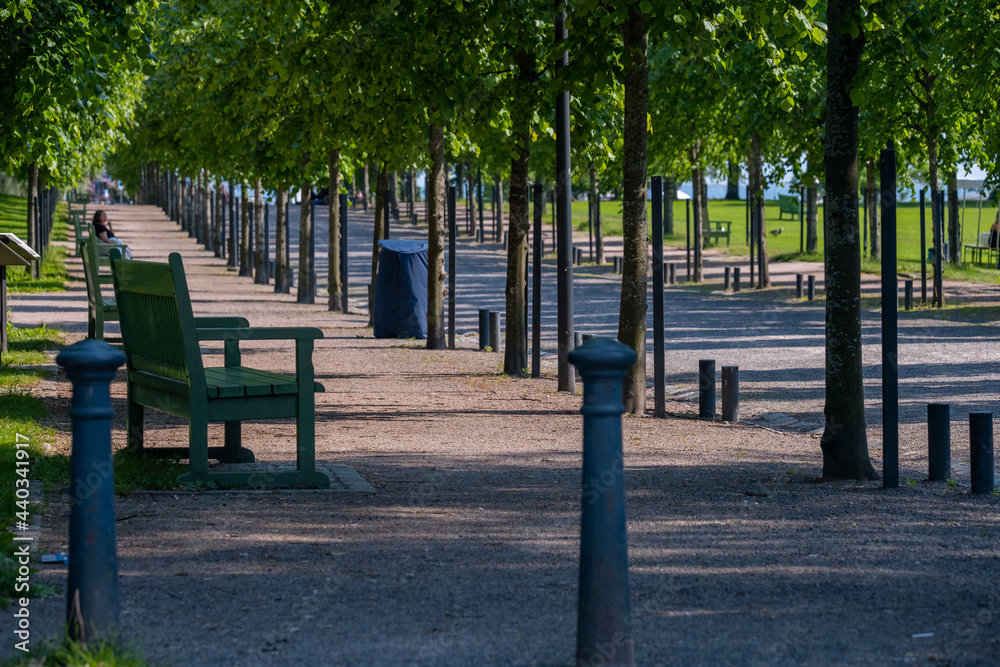 Closeup of a metallic park bench in a public park. An out of focus person sitting in the background. Closeup of a metallic park bench in a public park. An out of focus person sitting in the background.