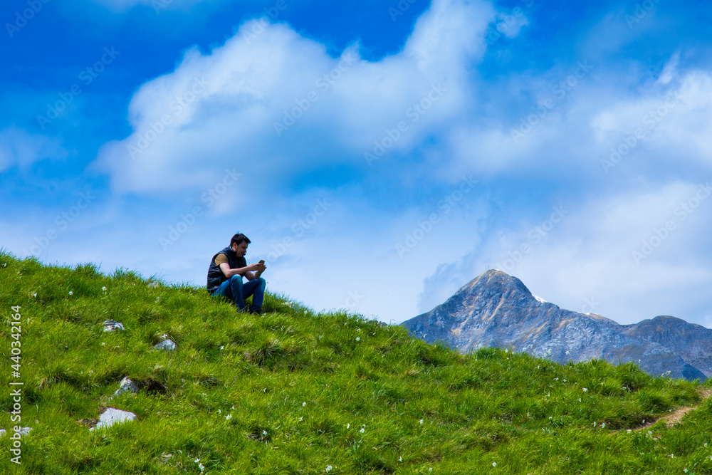 man sitting on the top of the flowered mountain and looks at the phone