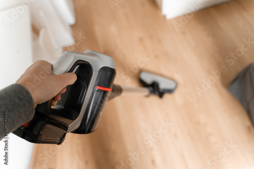 Cleaning wooden floor with wireless vacuum cleaner. Handheld cordless cleaner. Household appliance. Housework modern equipment