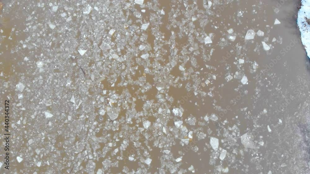 Aerial view of the course of the ice on the river. People stand on the bridge over the river and watch the ice float down the river. Ice has broken into many pieces and the stormy river is carrying it