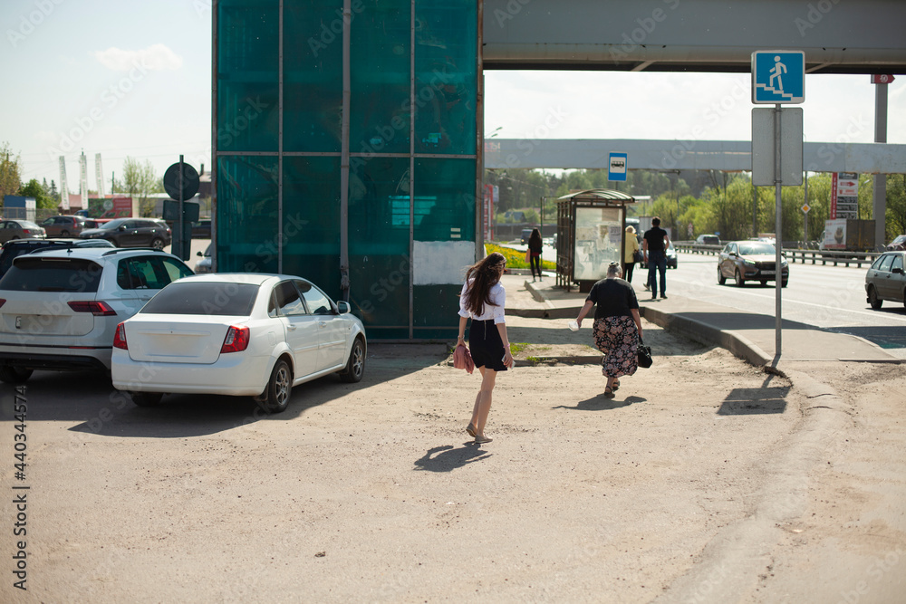 The girl walks along the side of the road. A girl in a skirt walks down the street.