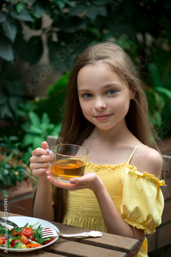 Cute little girl is drinking tea on breakfast. Kid holds hot beverage