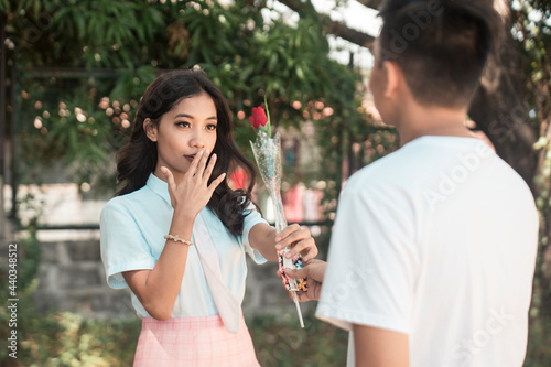 A petite young asian woman is surprised to receive a rose from a secret admirer who confesses his feelings for her. Outdoor scene.
