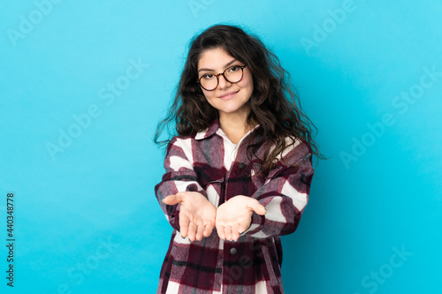 Teenager Russian girl isolated on blue background holding copyspace imaginary on the palm to insert an ad © luismolinero