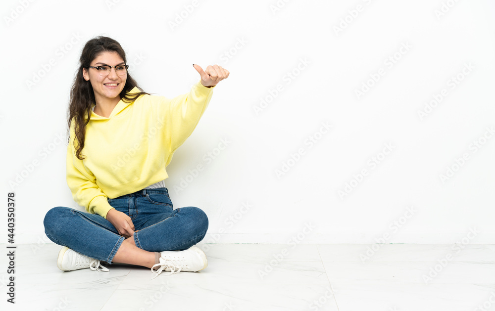 Teenager Russian girl sitting on the floor giving a thumbs up gesture Teenager Russian girl sitting on the floor giving a thumbs up gesture