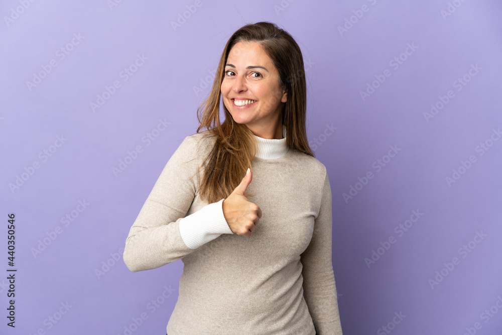 Middle age Brazilian woman isolated on purple background giving a thumbs up gesture