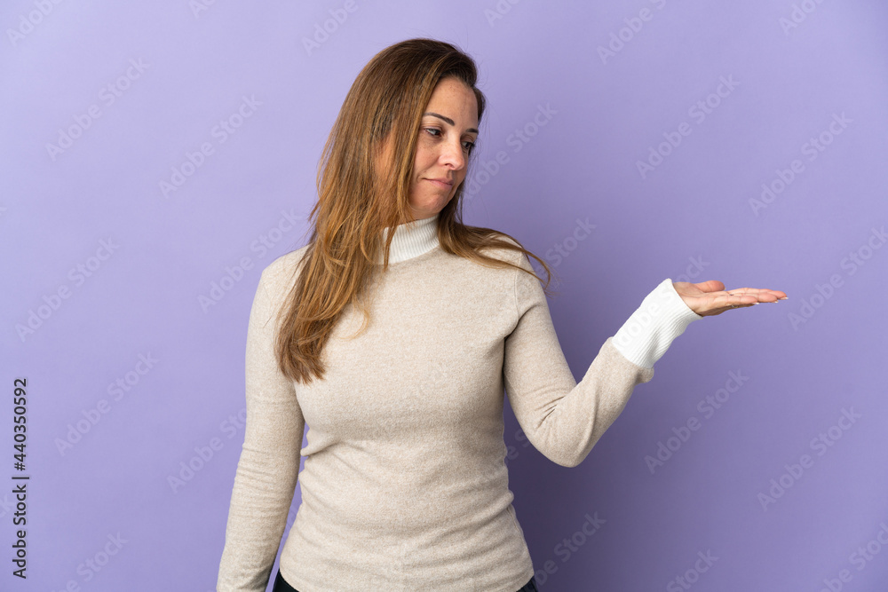 Middle age Brazilian woman isolated on purple background holding copyspace with doubts