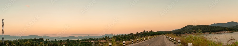 Asphalt road through the grass field and reservoir in the morning time. Panorama picture