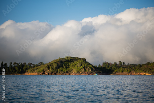 View from a boat of a big cloud sitting behind an island.