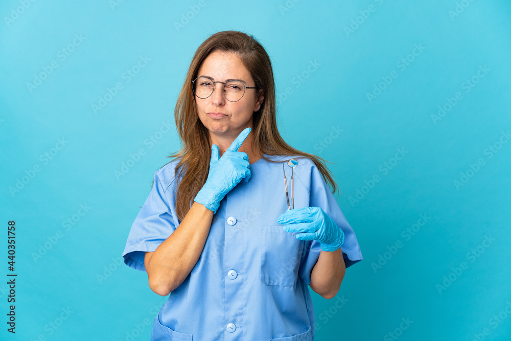 Middle age dentist Brazilian woman holding tools over isolated background having doubts while looking up Middle age dentist Brazilian woman holding tools over isolated background having doubts while looking up
