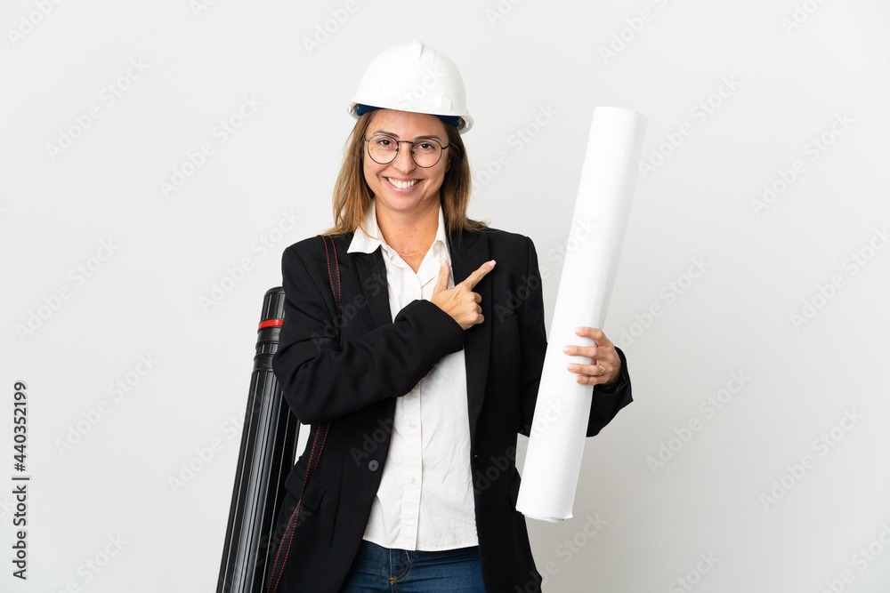 Middle age architect woman with helmet and holding blueprints over isolated background pointing to the side to present a product Middle age architect woman with helmet and holding blueprints over isolated background pointing to the side to present a product