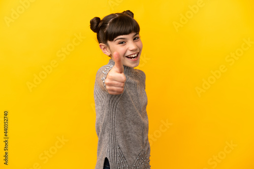 Little caucasian girl isolated on yellow background with thumbs up because something good has happened