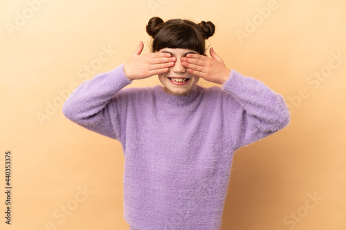 Little caucasian girl isolated on beige background covering eyes by hands and smiling