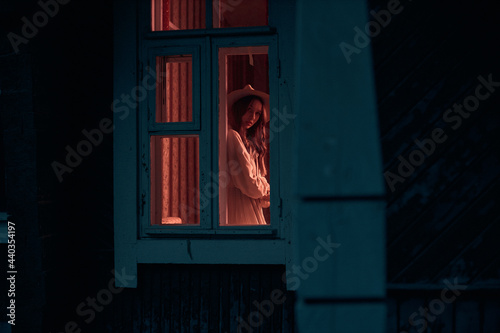 photo from the street to the mysterious girl who stands in the window, in a room with the lights on. Creative photography. High quality photo