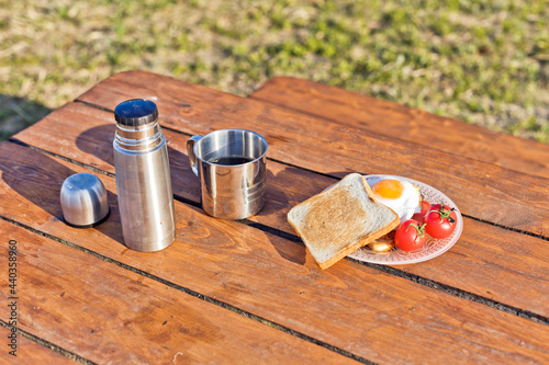 Breakfast in nature. Fried sandwich with egg, bacon, tomatoes and hot coffee from a thermos