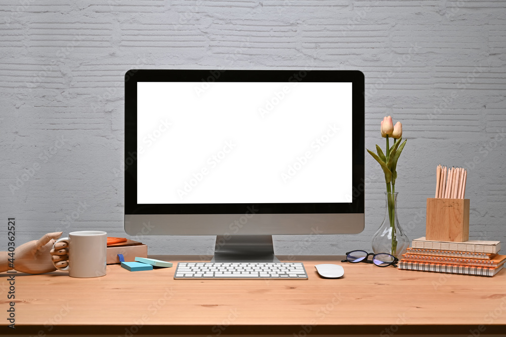 Fototapeta premium Mock up computer with stationery and coffee cup on wooden desk with brick wall.