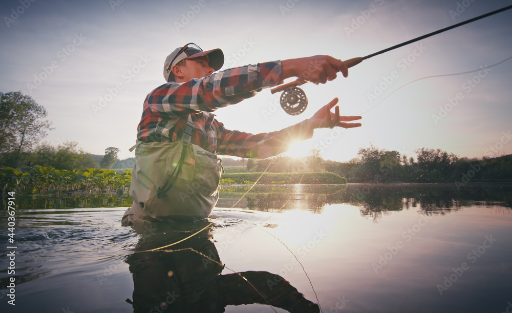 Fly fisherman stands in the water and casts the fly with fishing rod using  Roll Cast with lot of splashes Stock Photo