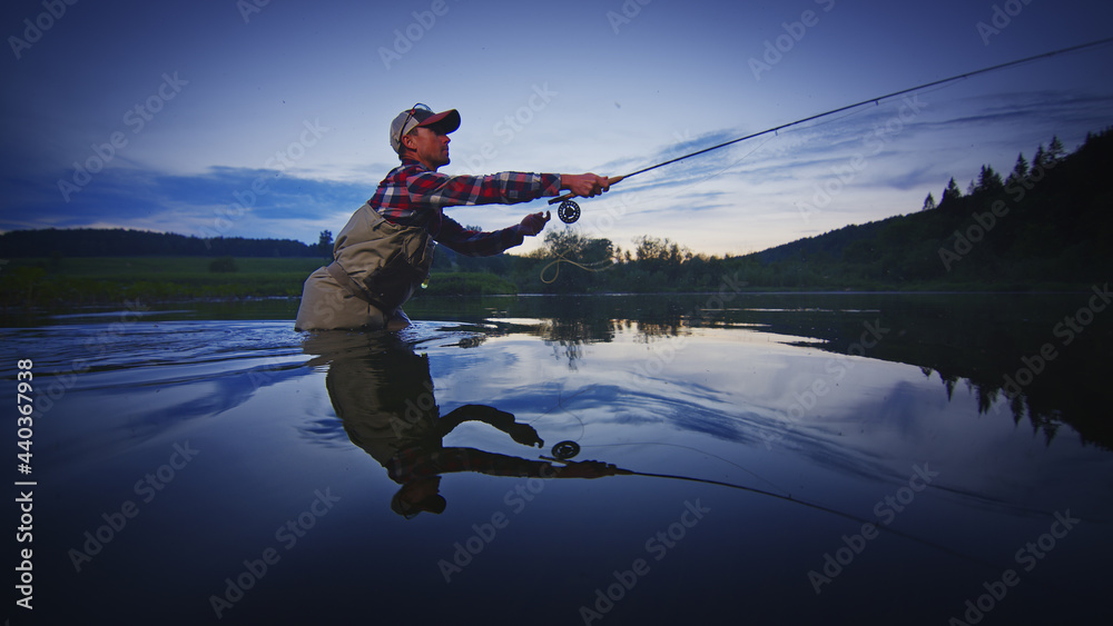 Fly fisherman stands in the water and fishing on the river at twilight Fly fisherman stands in the water and fishing on the river at twilight