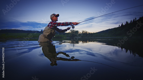 Fotografia, Obraz Fly fisherman stands in the water and fishing on the river at twilight